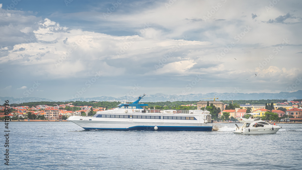 Passenger ferry leaving Zadar bay to sail on Adriatic Sea. Urban coastline with mountain range, Dinaric Alps, in background, Croatia