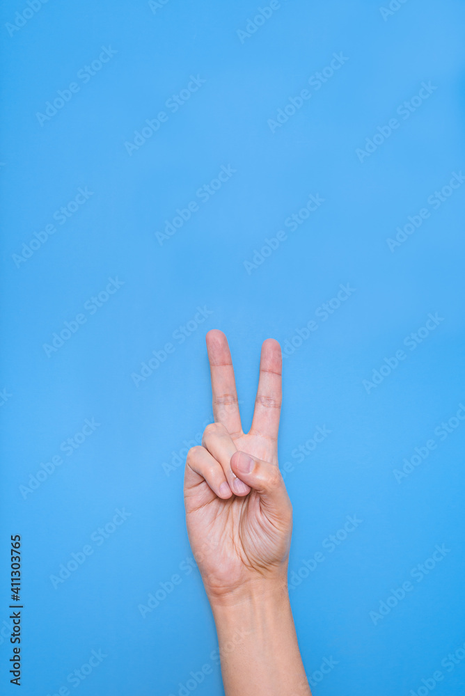 hand of a caucasian man doing victory symbol with fingers with blue background hand of a caucasian man doing victory symbol with fingers with blue background