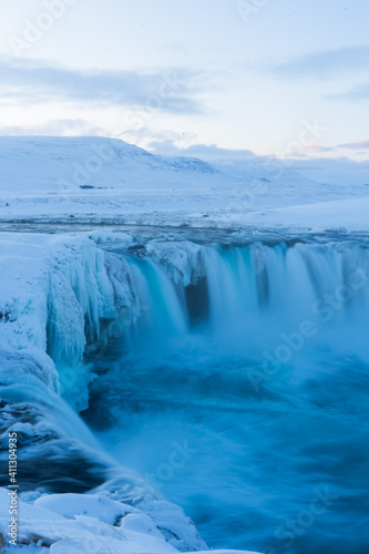 Scenic landscape view of tourist popular attraction Godafoss waterfall in northern Iceland in winter time. Long exposure falling water photo, snow covered mountains on background. 