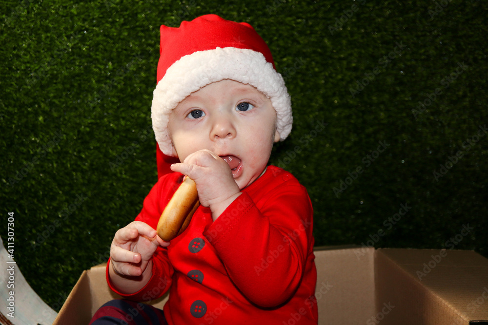 Fototapeta premium christmas gift - cute smiling child in red santa hat in the cardboard box eating the bagel