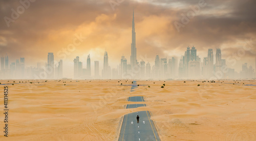 Принти на полотні View from above, stunning aerial view of an unidentified person walking on a deserted road covered by sand dunes with the Dubai Skyline in the background