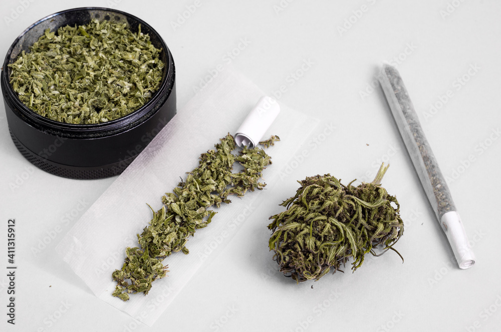Fototapeta premium grinder full of dry herb and joint with medical marijuana with paper filter and piece of rolling paper on white background