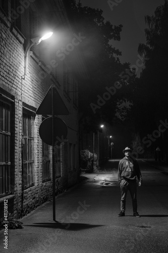 black and white portrait of a man with a huti on the street at night when lanterns are lit and the facade of the building with windows is visible