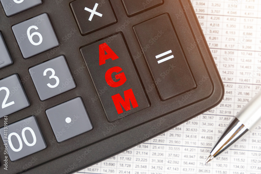 On the table is a report, a pen and a calculator, on the big key of which is written - AGM On the table is a report, a pen and a calculator, on the big key of which is written - AGM