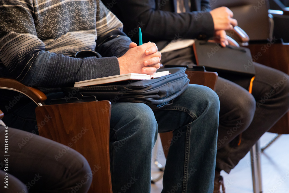 Men at a meeting or conference sit on chairs with sheets of paper and a ballpoint pen in their hands. Men at a meeting or conference sit on chairs with sheets of paper and a ballpoint pen in their hands.