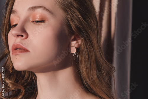 Portrait of a beautiful woman with a nude make-up and long curly hair in the studio. Fashion photography concept