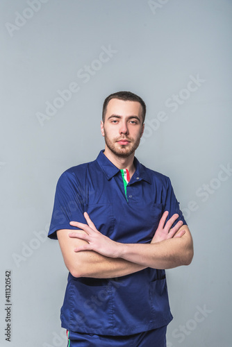 A young man in medical clothes and a robe sits in the studio on a gray background. Medical treatment and healthcare concept © Валентина Баранова