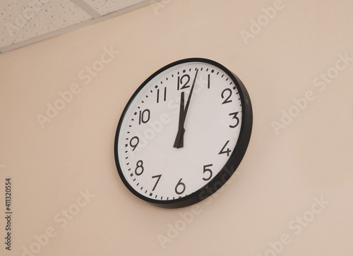 A large round indoor clock on the wall shows 12 o'clock.