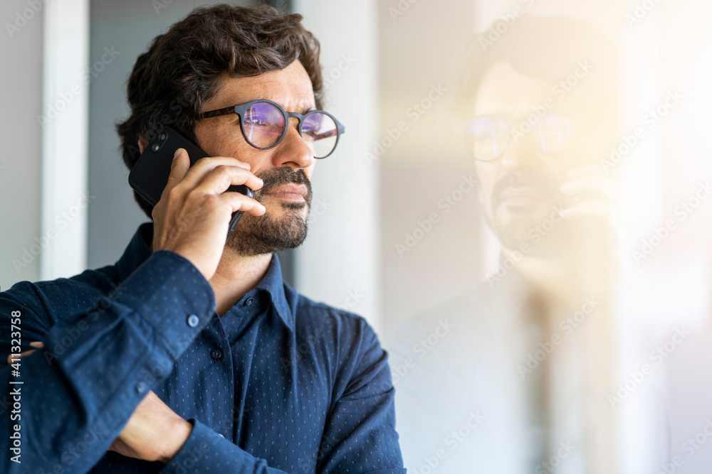 Casual man wearing glasses talking on the phone. Successful male portrait at the office by the window Casual man wearing glasses talking on the phone. Successful male portrait at the office by the window