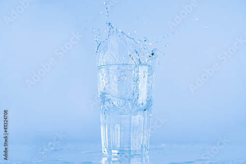 A glass of water splashed up. The water rose from a clear glass with a square.