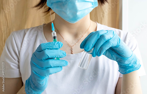 Nurse holds a syringe with a vaccine in her hand. Liquid in a syringe. Vaccination and healthcare. Medical concept. Doctor in gloves and a protective mask
