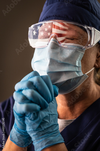American Flag Reflecting on Distressed Praying Female Medical Worker Wearing Protective Face Mask and Goggles