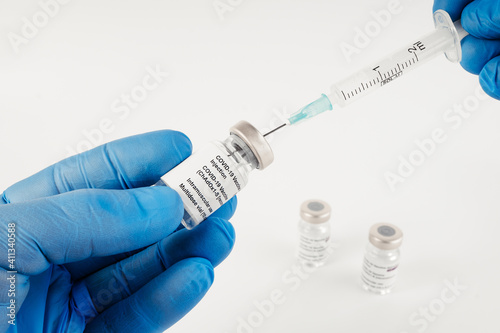 Blue gloves with three Covid-19 vaccine vials with white background and a syringe to inject medical professionals and people at risk.. SARS-CoV-2 vaccination treatment. Copy space.