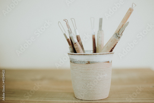 Tools of a craftsman (craft tools) in a ceramic cup, in a clear and white environment on a wooden table