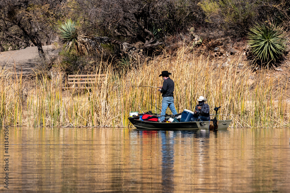 Two people fish from a small boat at Patagonia Lake State Park, Arizona. Both men are wearing face coverings. Their boat is overfilled with gear. Concepts of outdoor recreation, fishing, state parks Two people fish from a small boat at Patagonia Lake State Park, Arizona. Both men are wearing face coverings. Their boat is overfilled with gear. Concepts of outdoor recreation, fishing, state parks