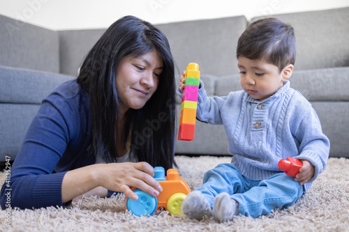 Mexican mother playing with son on carpet at home