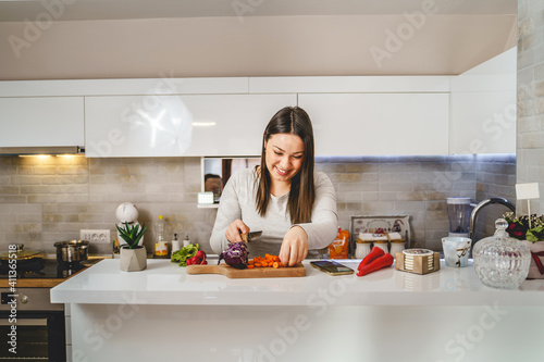 Front view portrait of adult caucasian woman in the kitchen cutting vegetables for vegan or vegetarian meal - Real people domestic life cooking healthy modern living concept