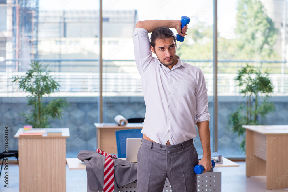 Young male employee doing sport exercises in the office