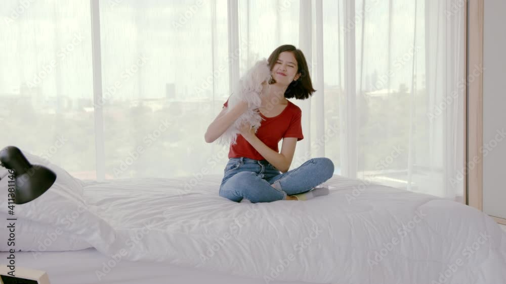 Wide Shot, Handheld, slow motion - Young mixed race lady sitting in bed, holding and kissing her cute little Maltese pet dog. New normal isolation activity for per lover. Wide Shot, Handheld, slow motion - Young mixed race lady sitting in bed, holding and kissing her cute little Maltese pet dog. New normal isolation activity for per lover.