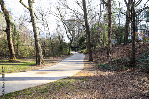 A shot of a long smooth concrete bike trail in the park surrounded by lush green trees and bare tree branches at Tanyard Creek Park in the Buckhead area of Atlanta Georgia photo