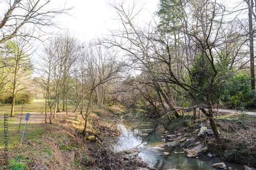 A shot of the still green creek waters with lush green trees and bare tree branches along the banks of the creek with lush green grass at Tanyard Creek Park in the Buckhead area of Atlanta Georgia photo