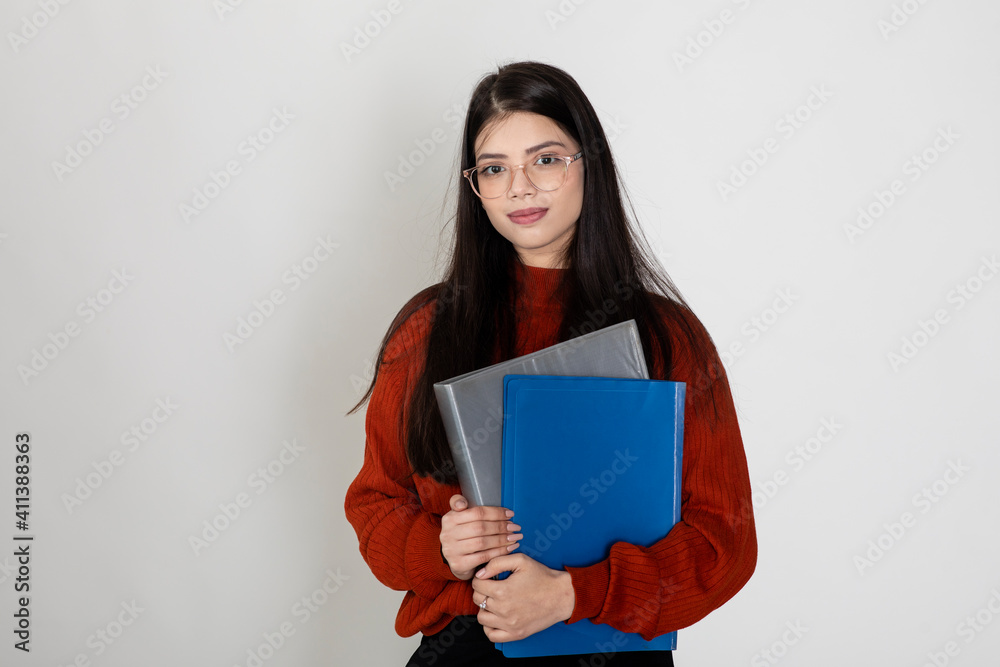 Portrait of a beautiful young lady wearing spectacles and holding business folders standing against white background, college student carrying files. Portrait of a beautiful young lady wearing spectacles and holding business folders standing against white background, college student carrying files.