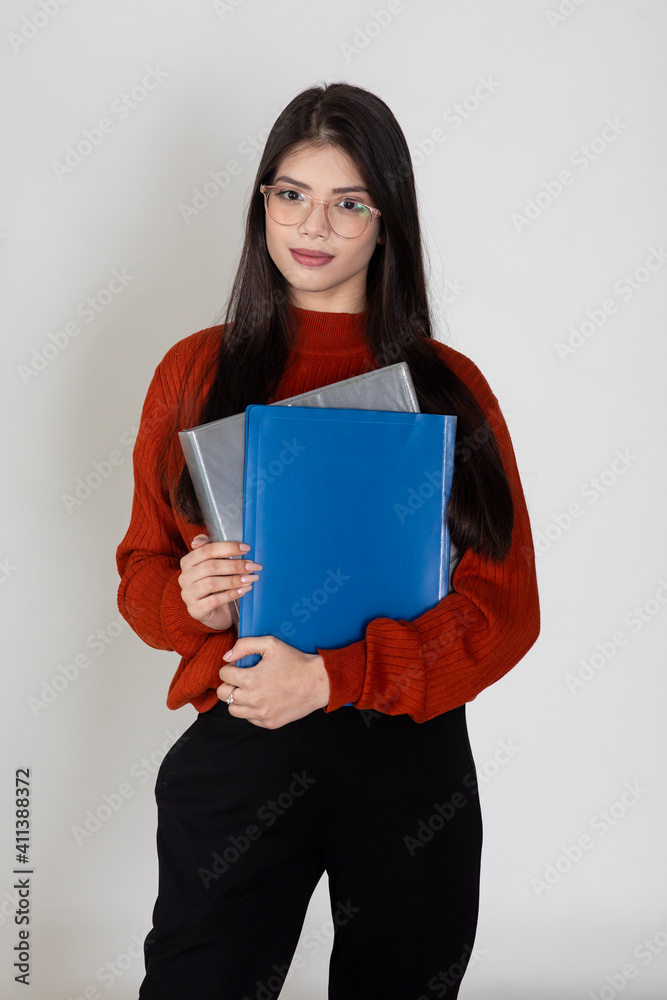 Portrait of a beautiful young lady wearing spectacles and holding business folders standing against white background, college student carrying files. Portrait of a beautiful young lady wearing spectacles and holding business folders standing against white background, college student carrying files.