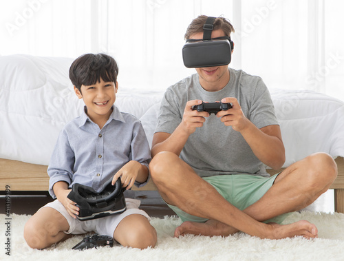 Father and his mixed-race son wearing vr virtual reality device to play a game together with fun and happy in bedroo