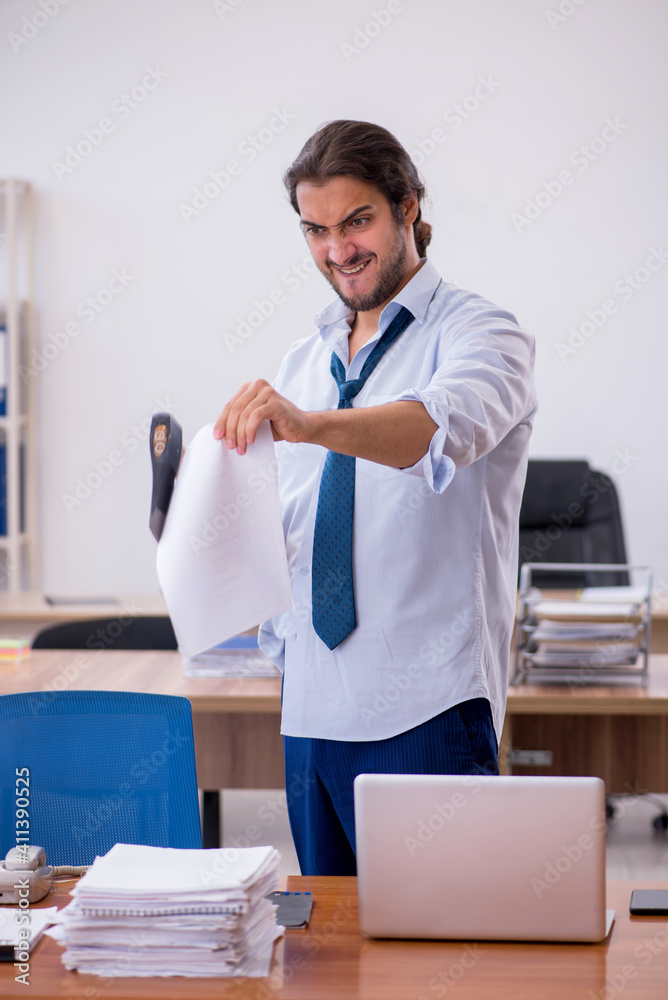 Young male furious employee holding hatchet in the office