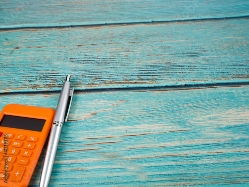 The orange calculator and pen on the wooden background. Business concept.