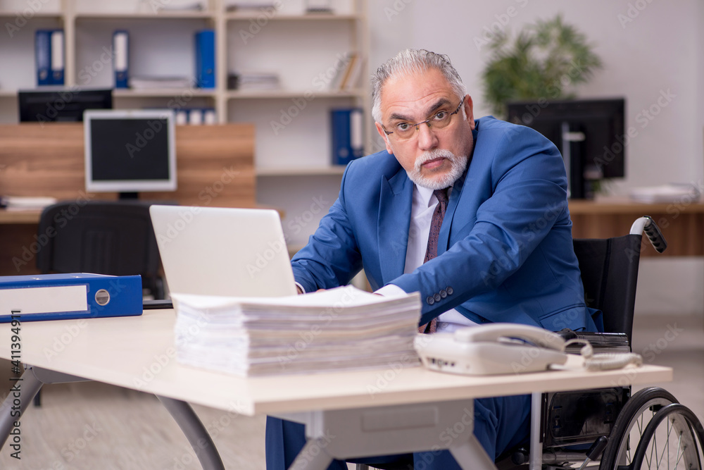 Old businessman employee in wheel-chair working in the office Old businessman employee in wheel-chair working in the office