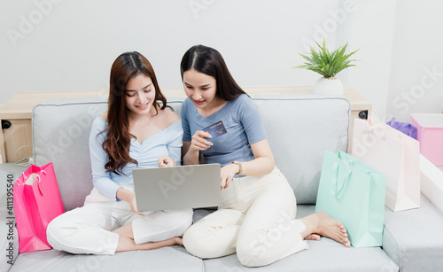 Two Asian beauty people are using a credit card to make purchases using a laptop via the internet. With a happy smiling face, being a new normal online business In the shopping experience from home