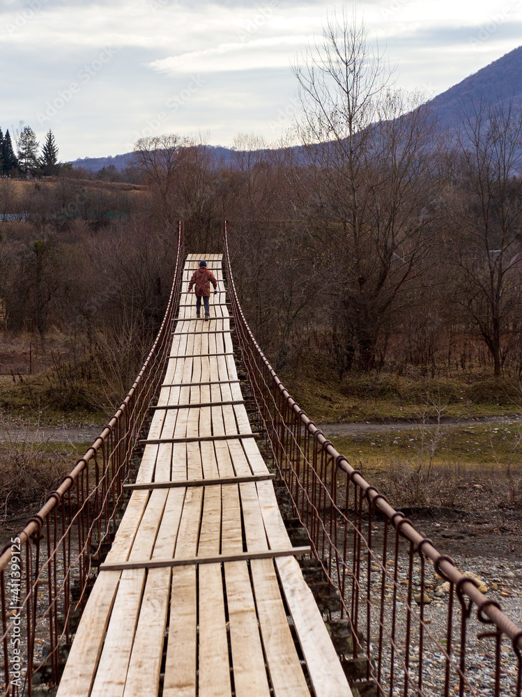 A suspension bridge on steel cables, temporary across a river in a mountainous area, in the autumn period of the year.