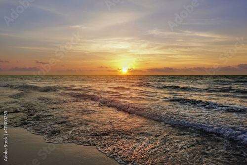 Dawn on the Caribbean coast. The rising sun colors the blue sky and clouds in golden tones. Waves roll onto the beach and leave openwork foam on the sand. Mexico