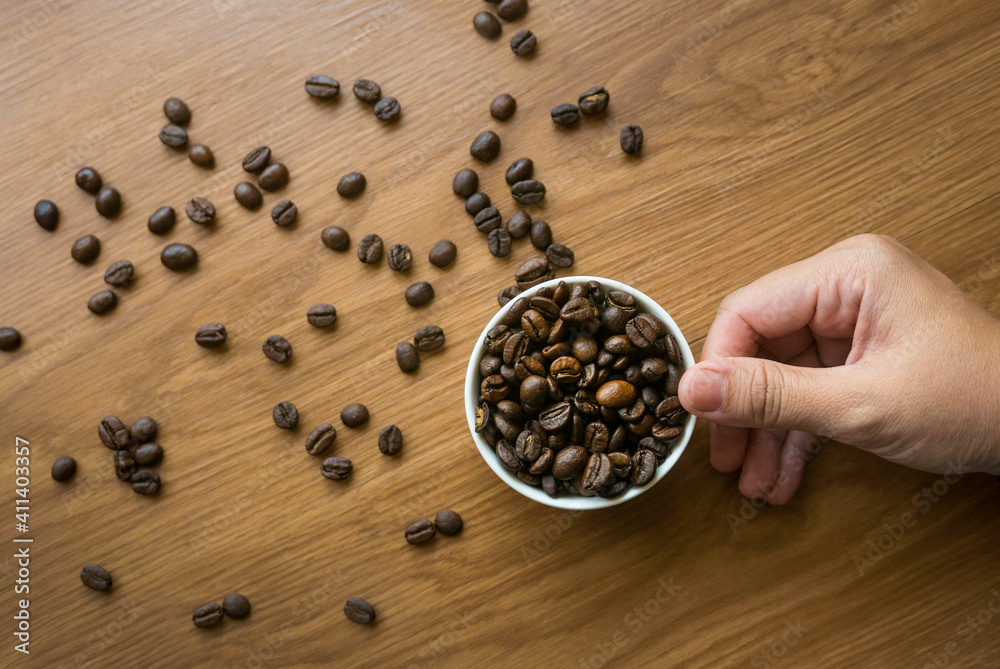 Selective focus of hand holding a cup full with coffee beans on wooden background. Selective focus of hand holding a cup full with coffee beans on wooden background.