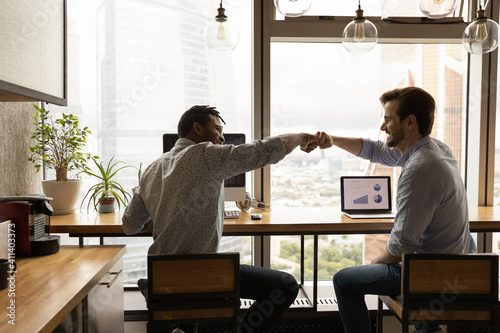 Well done, buddy. Motivated diverse young men coworkers bump fists on workplace feel excited achieve common goal. Two workers international business team members share success glad to help one another photo
