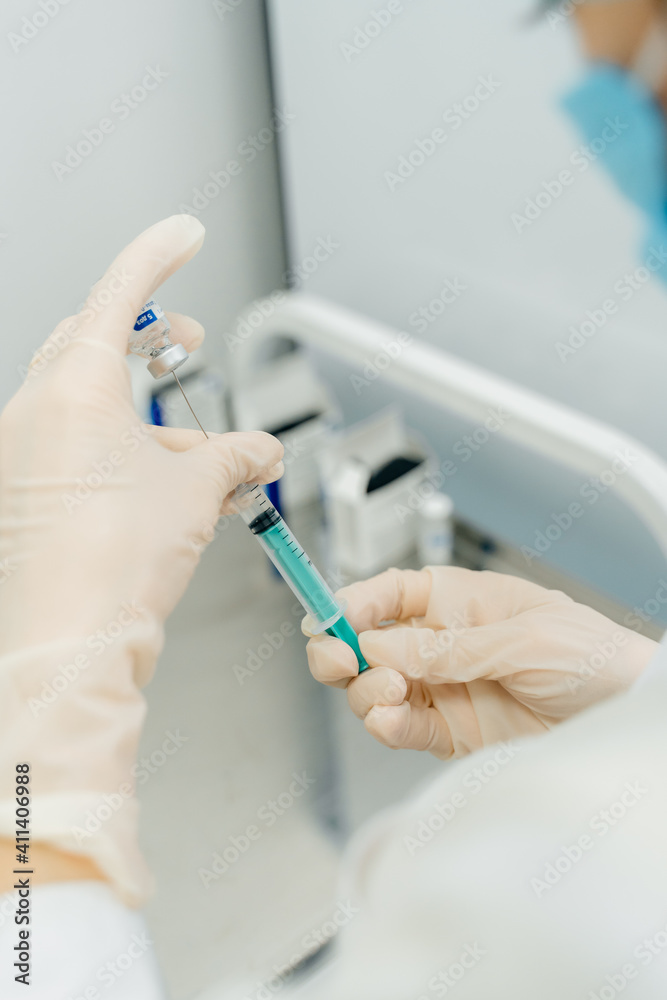 The nurse draws the vaccine into a syringe. Nurse's hands in white rubber gloves The nurse draws the vaccine into a syringe. Nurse's hands in white rubber gloves