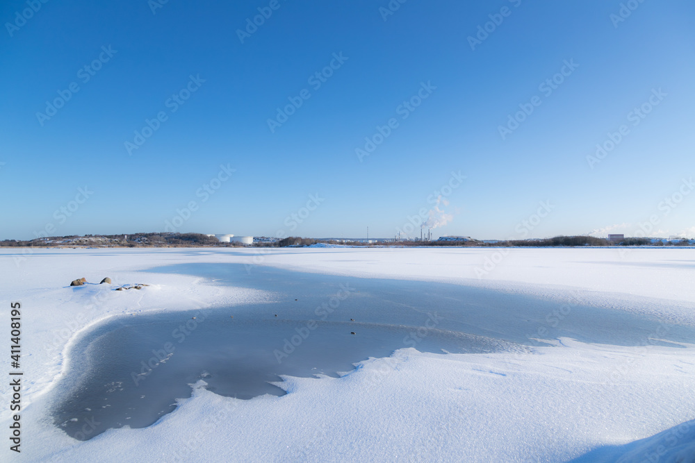 Naklejka premium Frozen sea on sunny day with chemical plants in the background. Gothenburg, Sweden 020621