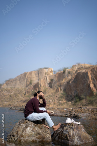Young indian traveler with long hair sitting near a lake with some books. travel and freedom concept.