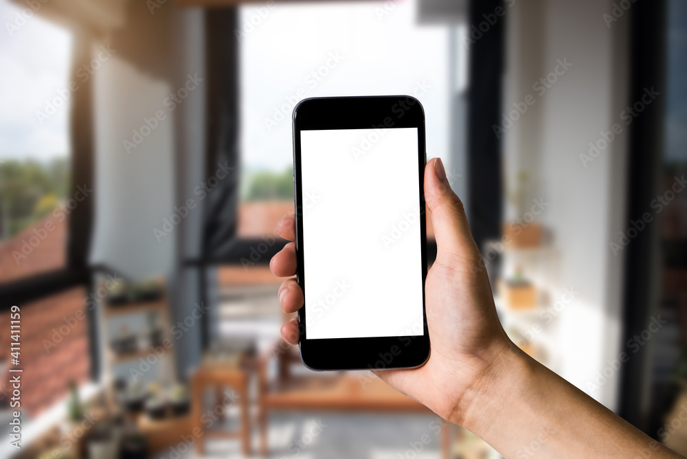 Hand holding white mobile phone with blank white screen in cafe. Hand holding white mobile phone with blank white screen in cafe.