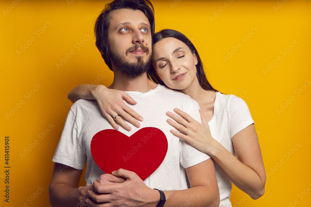 man and a woman in white T-shirts hold a paper heart in the studio on Valentine's Day