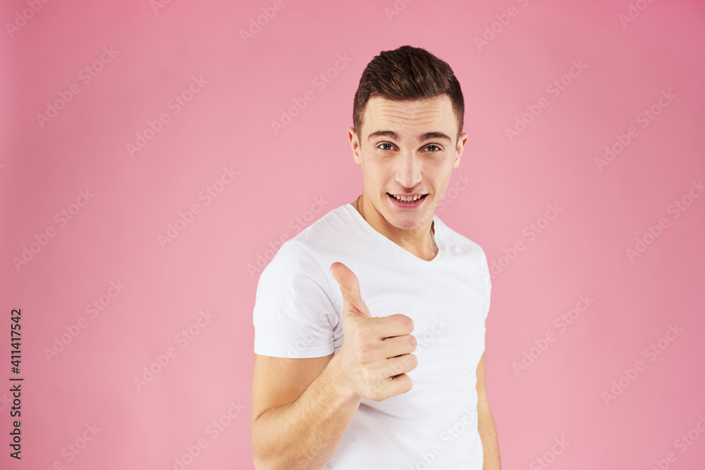 A man in a white t-shirt gestures with his hands emotions pink background studio cropped view