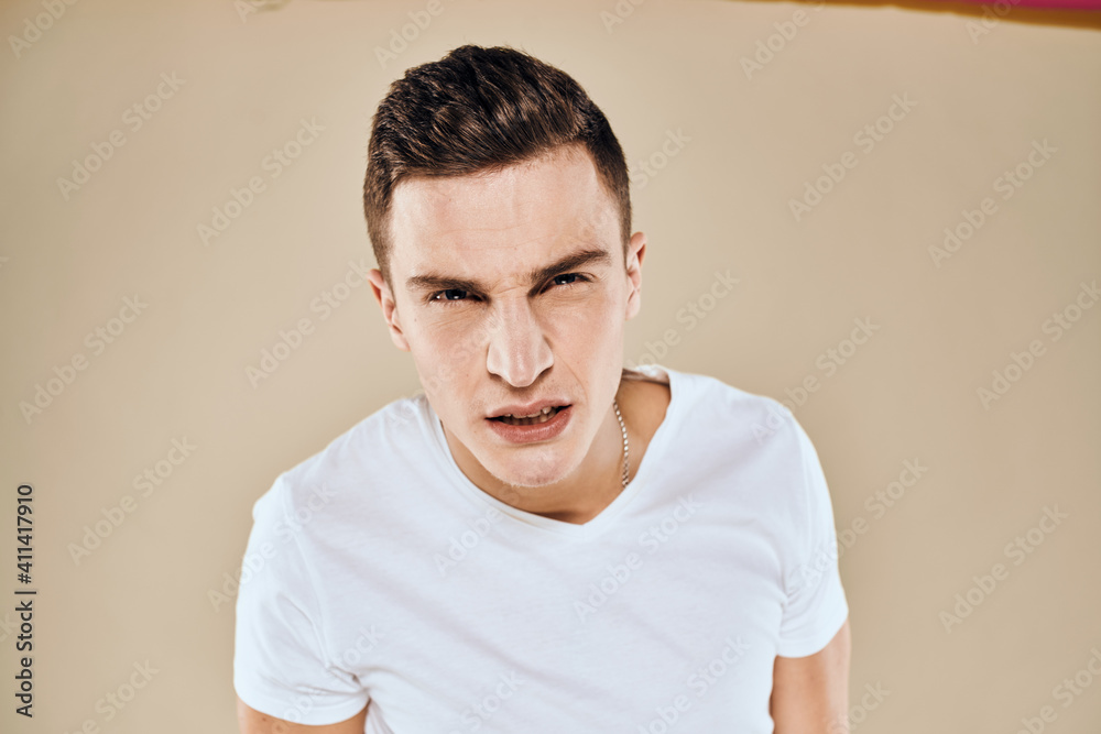 Man with displeased facial expression emotions white t-shirt gestures with hands beige background