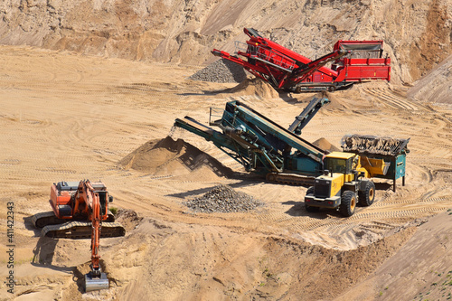 Mobile crushers and screens in open pit. Wheel front-end loader loads sand into mobile jaw crusher. Heavy machinery in the mining quarry, excavators and dump truck. Excavator on earthworks photo