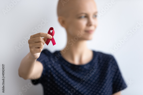 Crop close up blurred background of bald female patient show red ribbon breast cancer symbol sign. Young Caucasian hairless woman suffer from oncology fight beat illness. Support, awareness concept.
