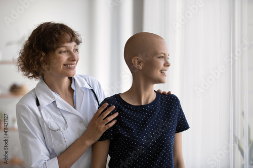 Smiling Caucasian doctor or nurse support comfort millennial woman struggle with oncology. Happy GP and optimistic female cancer patient look in distance dream of illness recovery or remission.