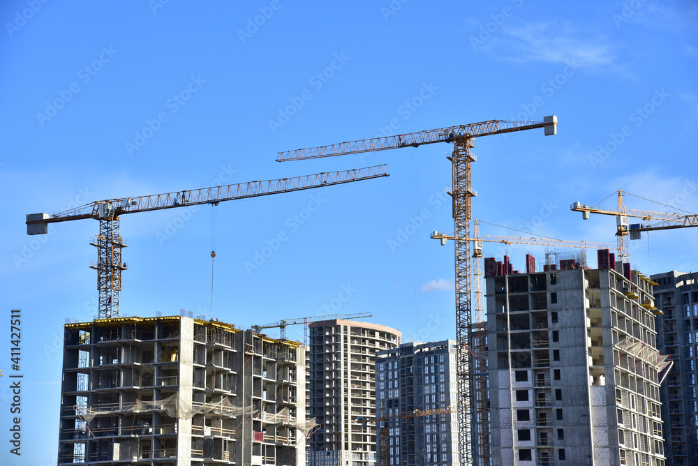 Crane at a construction site during the construction of residential buildings. Tower cranes against the blue sky. The concept of renovation and improvement of housing in the city
