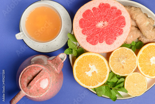 Tea cup and tea pot with cut citrus fruit over blue background. Tea time, healthy lemon and grapefruit drink concept.