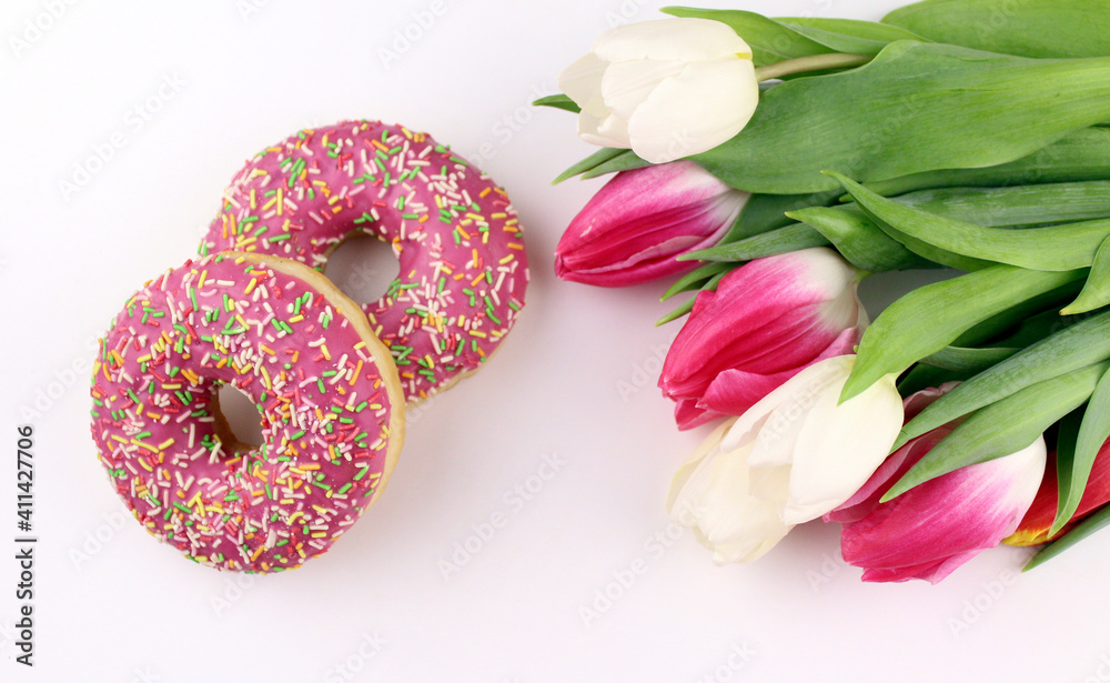 Pink donuts with a bouquet of tulips on a white background. Sweets with flowers. Gifts for the holidays Pink donuts with a bouquet of tulips on a white background. Sweets with flowers. Gifts for the holidays