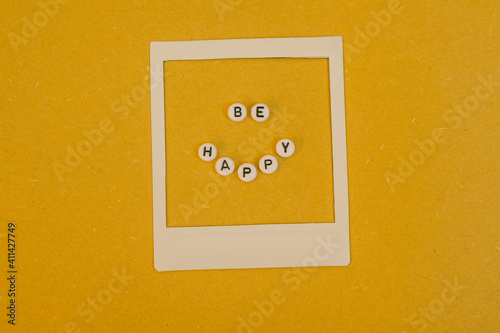 Text Be Happy in a Polaroid frame on yellow background. Concept happiness, positive mindset and optimism. 